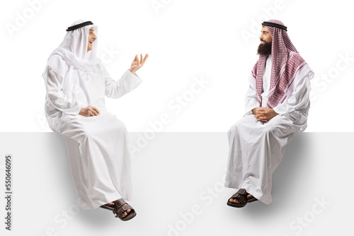 Two arab men seated on a white panel having a conversation