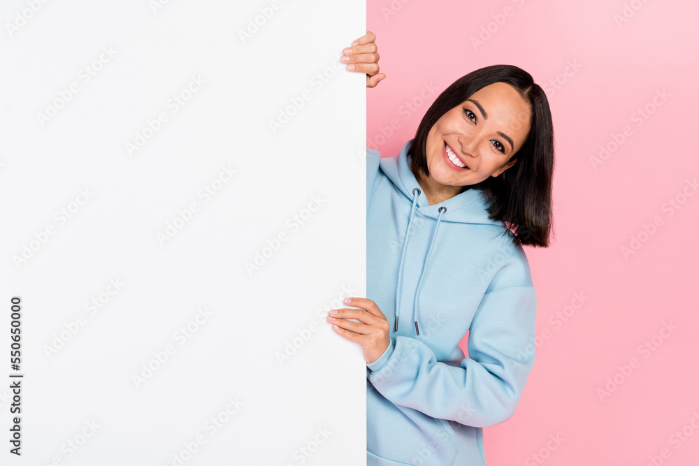 Photo of funny adorable lady wear blue hoodie holding white billboard empty space isolated pink color background Photo of funny adorable lady wear blue hoodie holding white billboard empty space isolated pink color background