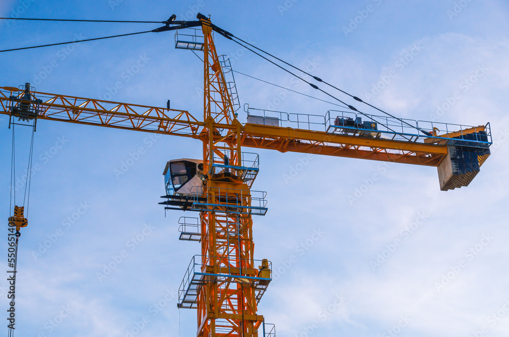 A tower construction crane on the background of a blue sky with clouds. Boom rotary crane with boom. Construction of apartment buildings in the city. Construction of high-rise buildings. A tower construction crane on the background of a blue sky with clouds. Boom rotary crane with boom. Construction of apartment buildings in the city. Construction of high-rise buildings.