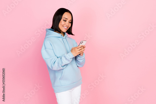 Photo of pretty cute lady wear blue hoodie communicating modern device empty space isolated pink color background