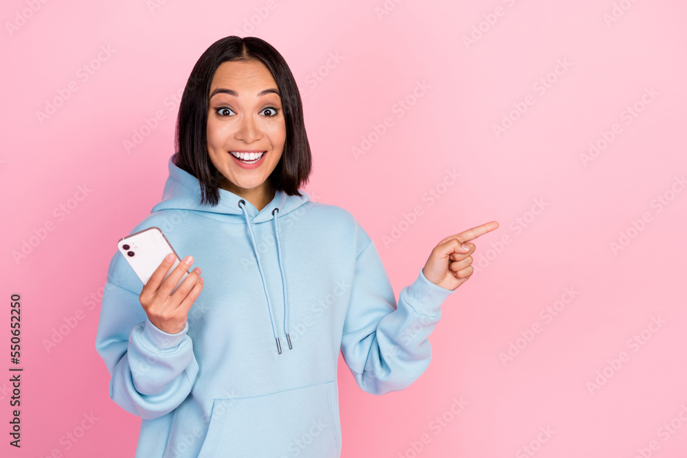 Photo of funny impressed girl dressed blue sweatshirt writing sms modern gadget pointing empty space isolated pink color background Photo of funny impressed girl dressed blue sweatshirt writing sms modern gadget pointing empty space isolated pink color background
