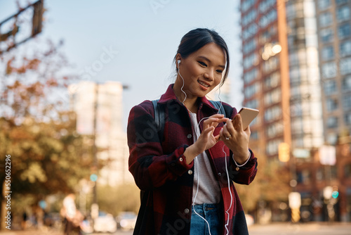 Young Asian student texting on her smart phone in city.