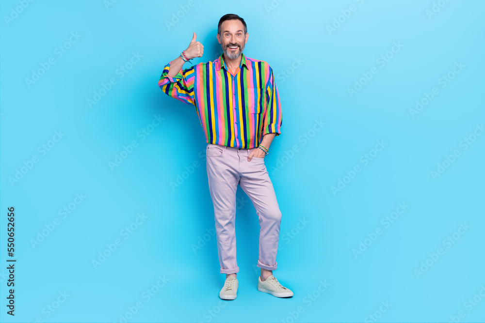 Full length photo of cheerful eccentric successful man hand thumb up positive feedback shop service isolated on blue color background Full length photo of cheerful eccentric successful man hand thumb up positive feedback shop service isolated on blue color background