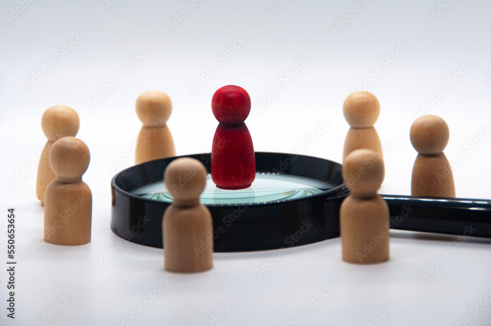 Obraz premium Red wooden doll on top of magnifying glass surrounded with other wooden figure. leadership concept