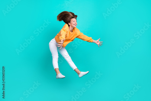 Fototapeta Naklejka Na Ścianę i Meble -  Full length photo of impressed schoolgirl wear sweatshirt jumping holding arms huge big object product isolated turquoise color background