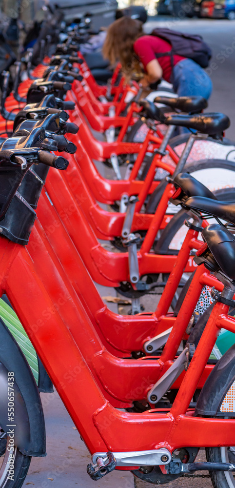 Detail of the handlebars and pedals of shared rental red bicycles parked in a row on a street in the city of Barcelona. Detail of the handlebars and pedals of shared rental red bicycles parked in a row on a street in the city of Barcelona.