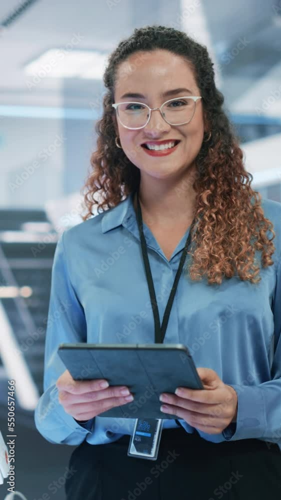Vertical Screen: Beautiful Hispanic Female Wearing Glasses, Using Tablet Computer, Looking at Camera and Smiling. Businesswoman, Information Technology Manager, Robotics Engineering Specialist. Vertical Screen: Beautiful Hispanic Female Wearing Glasses, Using Tablet Computer, Looking at Camera and Smiling. Businesswoman, Information Technology Manager, Robotics Engineering Specialist.