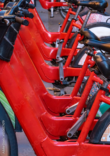 Detail of the handlebars and pedals of shared rental red bicycles parked in a row on a street in the city of Barcelona.