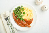 Bangers and mash. Grilled sausages with mash potato and green pea on white plate on light background. Traditional dish of Great Britain and Ireland. BBQ beef sausages. Top view.