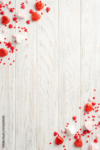 Valentine's Day mood concept. Top view vertical photo of heart shaped candies on white wooden desk background with copyspace