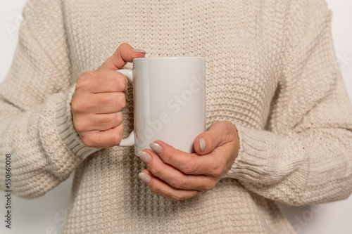 A woman in a white jumper is holding a white mug. The concept of comfort and warmth.