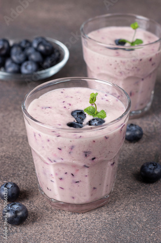 Homemade smoothie with blueberries in two glasses on brown background