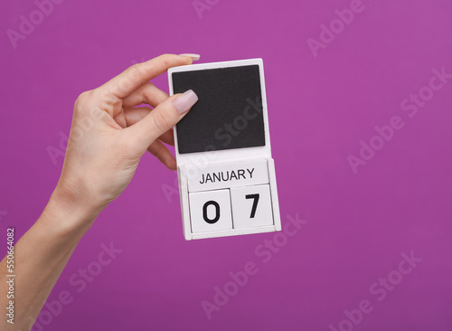 Female hand holding wooden calendar with date January 07 on purple background