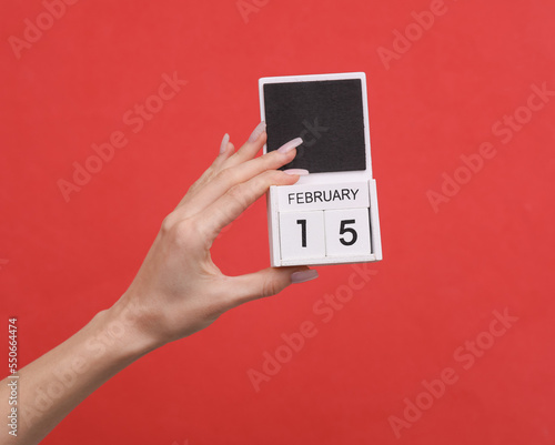 Female hand holding wooden calendar with date February 15 on red background
