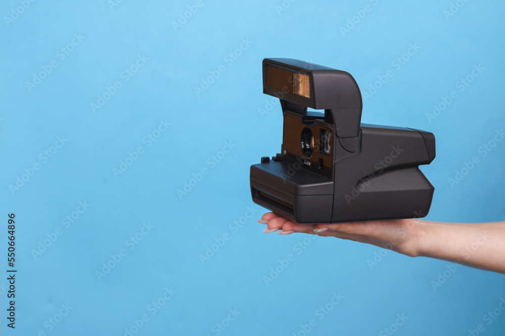 Female hand holding instant retro camera on blue background Female hand holding instant retro camera on blue background