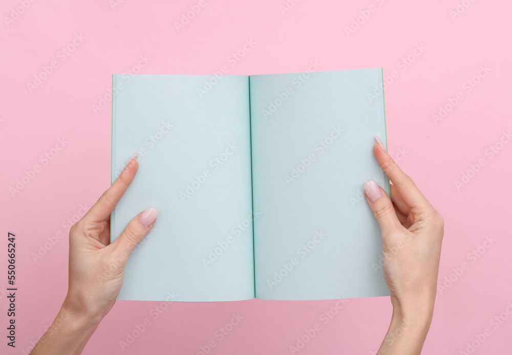 Obraz premium Female hands hold a notepad with blue sheets of paper on a pink pastel background.