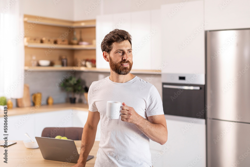 Smiling pensive mature caucasian man with beard in white t-shirt thinks, enjoys drink in cup, looks at free space Smiling pensive mature caucasian man with beard in white t-shirt thinks, enjoys drink in cup, looks at free space