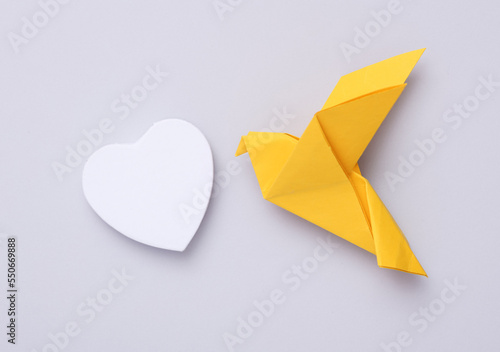 Yellow origami dove with heart on a gray background. Peace symbol, no war
