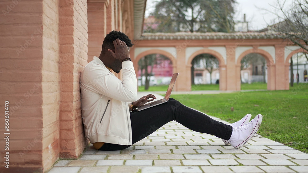 Young black man working remotely with laptop outside. African entrepreneur or student typing on computer2 Young black man working remotely with laptop outside. African entrepreneur or student typing on computer2