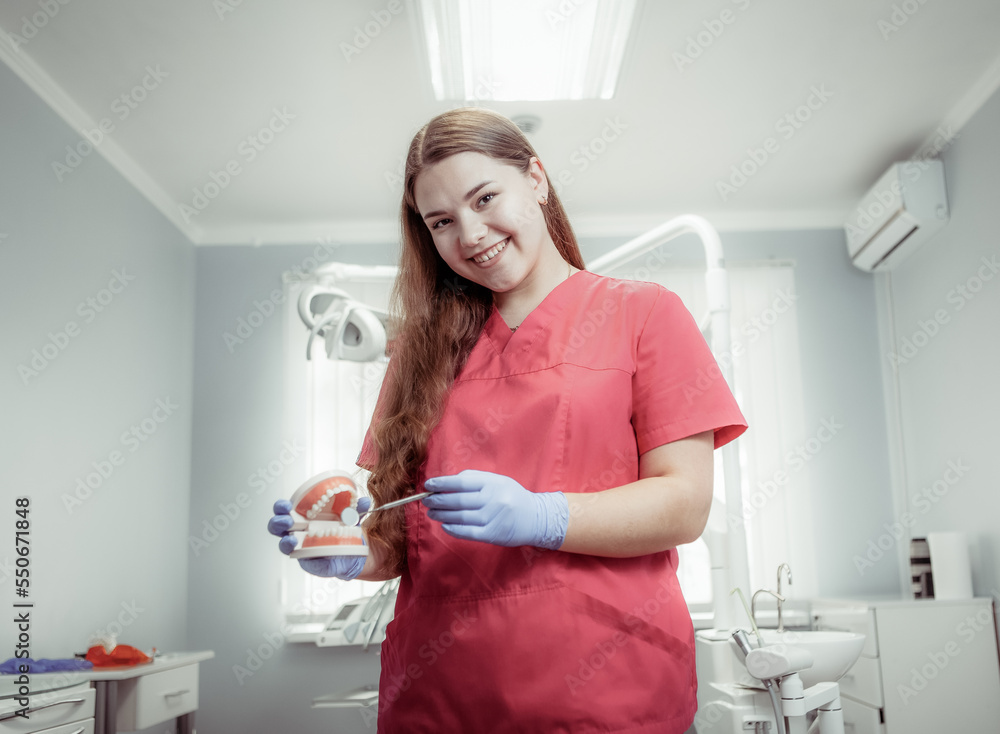 Portrait of smiling professional female dentist in red medical uniform at dentist office