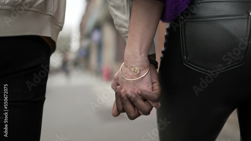Young black man and white woman holding hands walking outside in city together. Interracial couple lovers