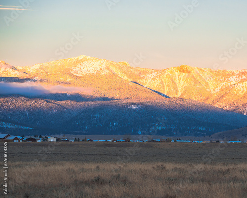 The sunrise casts a golden glow on the snow capped mountains above a small town. 