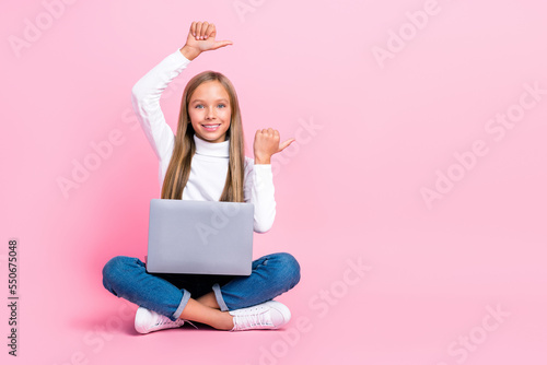 Full body portrait of cheerful girl sit floor use netbook indicate thumb fingers empty space isolated on pink color background © deagreez