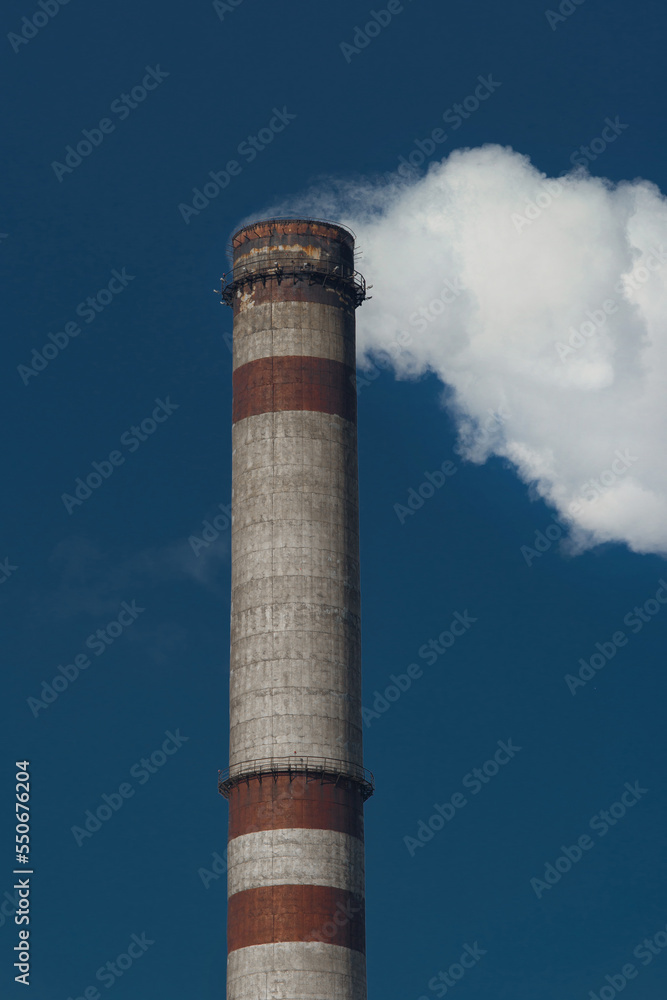 Pollution of the environment, ecology and air. Withdrawal of combustion products of soot, smoke and gases from the pipe of an industrial plant into the atmosphere against the background of a blue sky Pollution of the environment, ecology and air. Withdrawal of combustion products of soot, smoke and gases from the pipe of an industrial plant into the atmosphere against the background of a blue sky