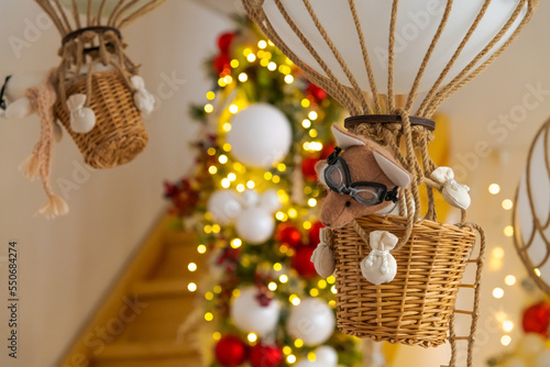 Small mouse in glasses stuffed toy flies in basket on air balloon. Blurred Christmas garland in the background. Selective focus. Copy space for your text. Christmas travek theme. photo