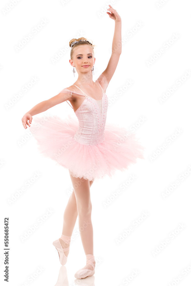 Young woman ballerina in white tutu, dancing on pointe with arms overhead, in the studio against a dark background. Young woman ballerina in white tutu, dancing on pointe with arms overhead, in the studio against a dark background.