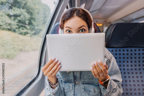 Girl with a funny emotion hiding behind her laptop notebook during a train ride. Personal data theft and Wi-Fi Internet and information security