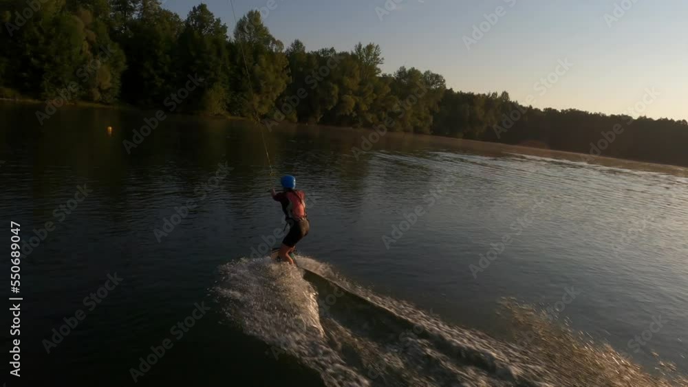 Cinematic FPV video of extreme young woman wakeboard surfer wearing helmet riding on lake water at cable wake park on background of bright sunlight at summer sunny day. Shooting in slow motion. Cinematic FPV video of extreme young woman wakeboard surfer wearing helmet riding on lake water at cable wake park on background of bright sunlight at summer sunny day. Shooting in slow motion.