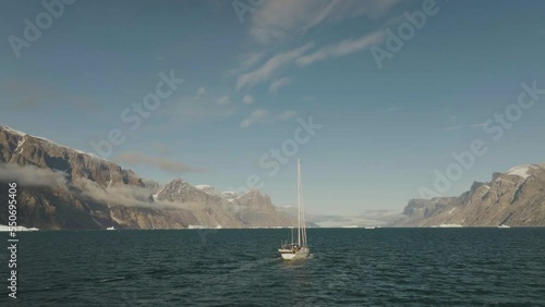 Aerial view of a sailing boat navigating along the fjords with iceberg near the coast, Sermersooq, Greenland. photo