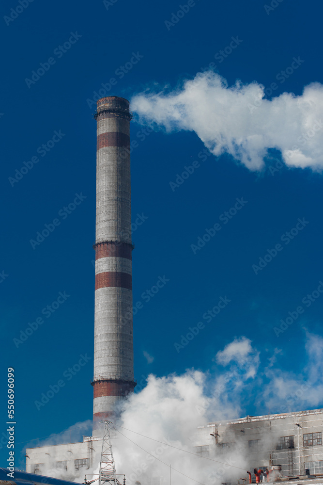 Pollution of the environment, ecology and air. Withdrawal of combustion products of soot, smoke and gases from the pipe of an industrial plant into the atmosphere against the background of a blue sky Pollution of the environment, ecology and air. Withdrawal of combustion products of soot, smoke and gases from the pipe of an industrial plant into the atmosphere against the background of a blue sky
