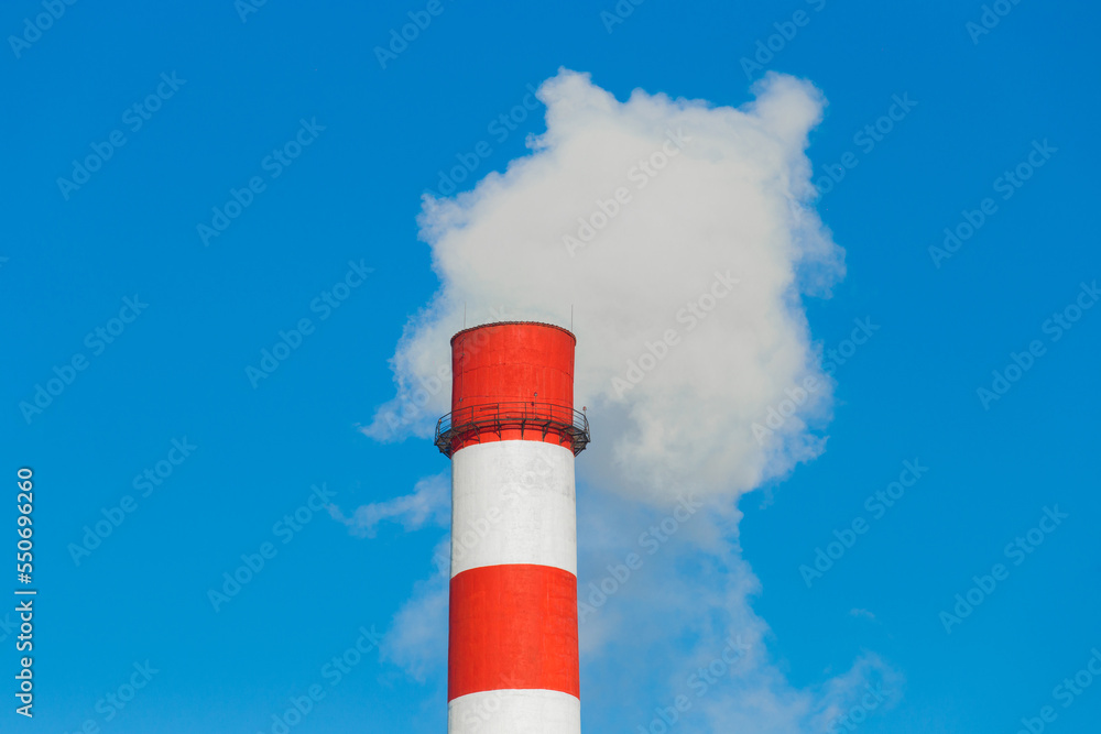 Pollution of the environment, ecology and air. Withdrawal of combustion products of soot, smoke and gases from the pipe of an industrial plant into the atmosphere against the background of a blue sky Pollution of the environment, ecology and air. Withdrawal of combustion products of soot, smoke and gases from the pipe of an industrial plant into the atmosphere against the background of a blue sky