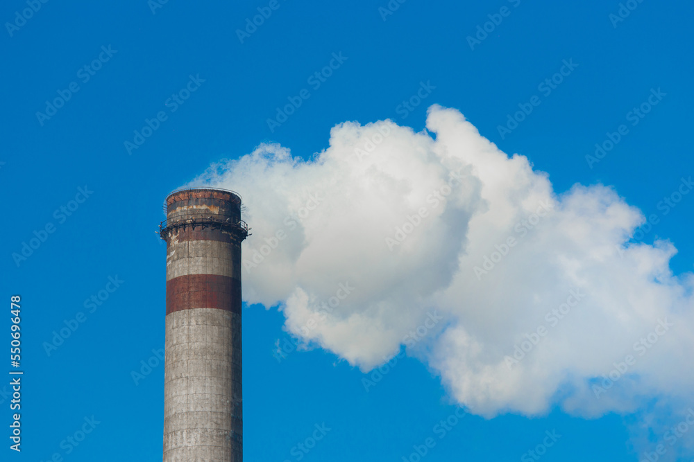 Pollution of the environment, ecology and air. Withdrawal of combustion products of soot, smoke and gases from the pipe of an industrial plant into the atmosphere against the background of a blue sky Pollution of the environment, ecology and air. Withdrawal of combustion products of soot, smoke and gases from the pipe of an industrial plant into the atmosphere against the background of a blue sky