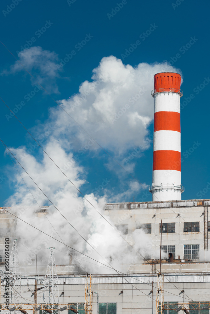 Pollution of the environment, ecology and air. Withdrawal of combustion products of soot, smoke and gases from the pipe of an industrial plant into the atmosphere against the background of a blue sky Pollution of the environment, ecology and air. Withdrawal of combustion products of soot, smoke and gases from the pipe of an industrial plant into the atmosphere against the background of a blue sky