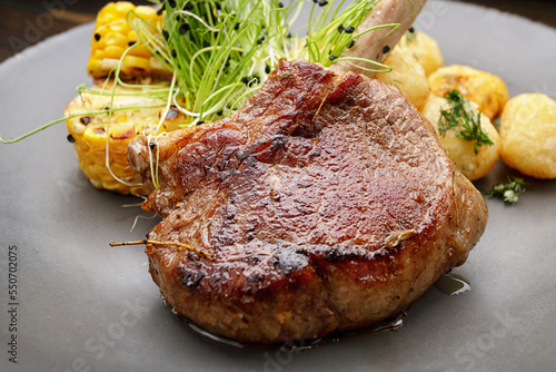 Фотография Veal entrecote with potatoes and corn, on a wooden background