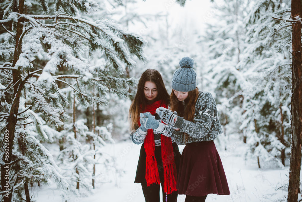 Close up fashion portrait of two sisters hugs and having fun, holding petard in winter time forest, wearing sweaters and scarfs,best friends couple outdoors, snowy weather Close up fashion portrait of two sisters hugs and having fun, holding petard in winter time forest, wearing sweaters and scarfs,best friends couple outdoors, snowy weather