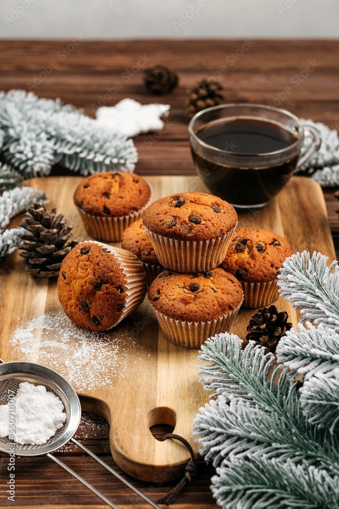 
muffins with chocolate on a wooden stand, powdered sugar, cones, Christmas tree branches nearby