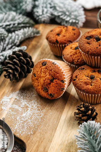 
muffins with chocolate on a wooden stand, powdered sugar, cones, Christmas tree branches nearby