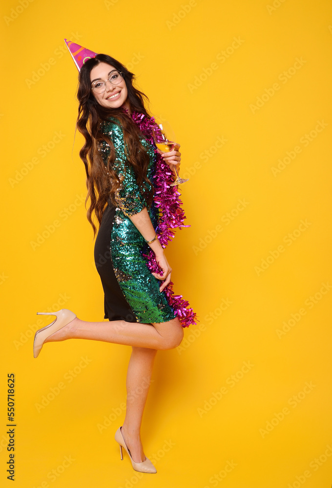 woman in a smart dress in a party cap with a pink boa around her neck and a glass of champagne smiling on a yellow background woman in a smart dress in a party cap with a pink boa around her neck and a glass of champagne smiling on a yellow background