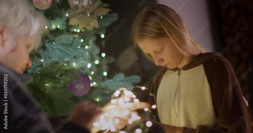 An elderly active woman unravels a garland near the New Year tree. Healthy and active lifestyle An elderly active woman unravels a garland near the New Year tree. Healthy and active lifestyle
