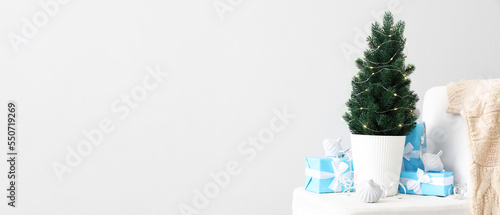 Small Christmas tree with presents and decor on chair near light wall