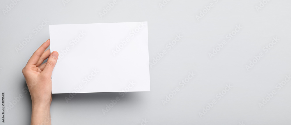 Female hand holding blank paper sheet on light background with space for text Female hand holding blank paper sheet on light background with space for text