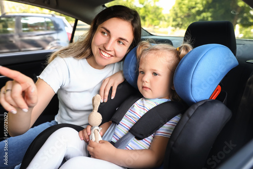 Mother and her little daughter with toy buckled in car safety seat © Pixel-Shot