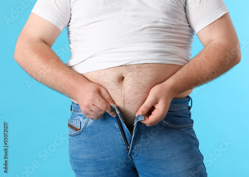 Young overweight man in tight jeans on blue background, closeup