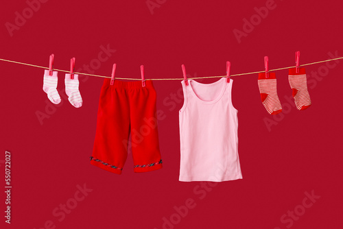 Stylish baby clothes hanging on rope against color background