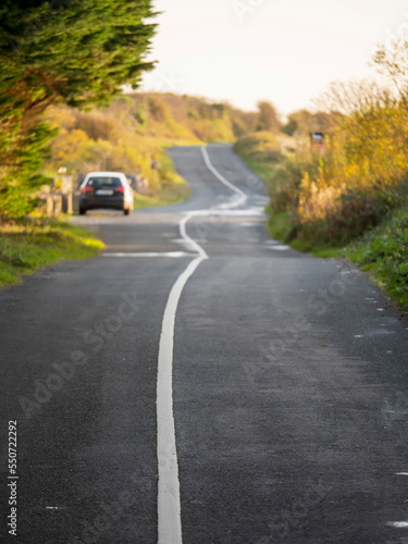 Small twisted asphalt road in a country side with a car parked off road. Selective focus. Travel and tourism concept.
