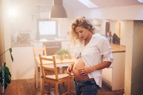 Portrait of pregnant woman standing at home holding hands on her belly © Zamrznuti tonovi